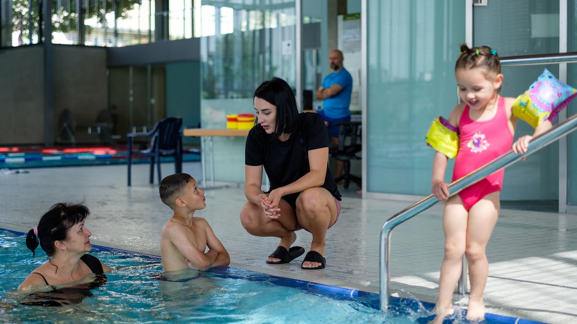 Alina (kniend am Becken) mit Tochter Polina, Sohn Max und Mutter Liubov, die beim Schwimmunterricht assistiert.