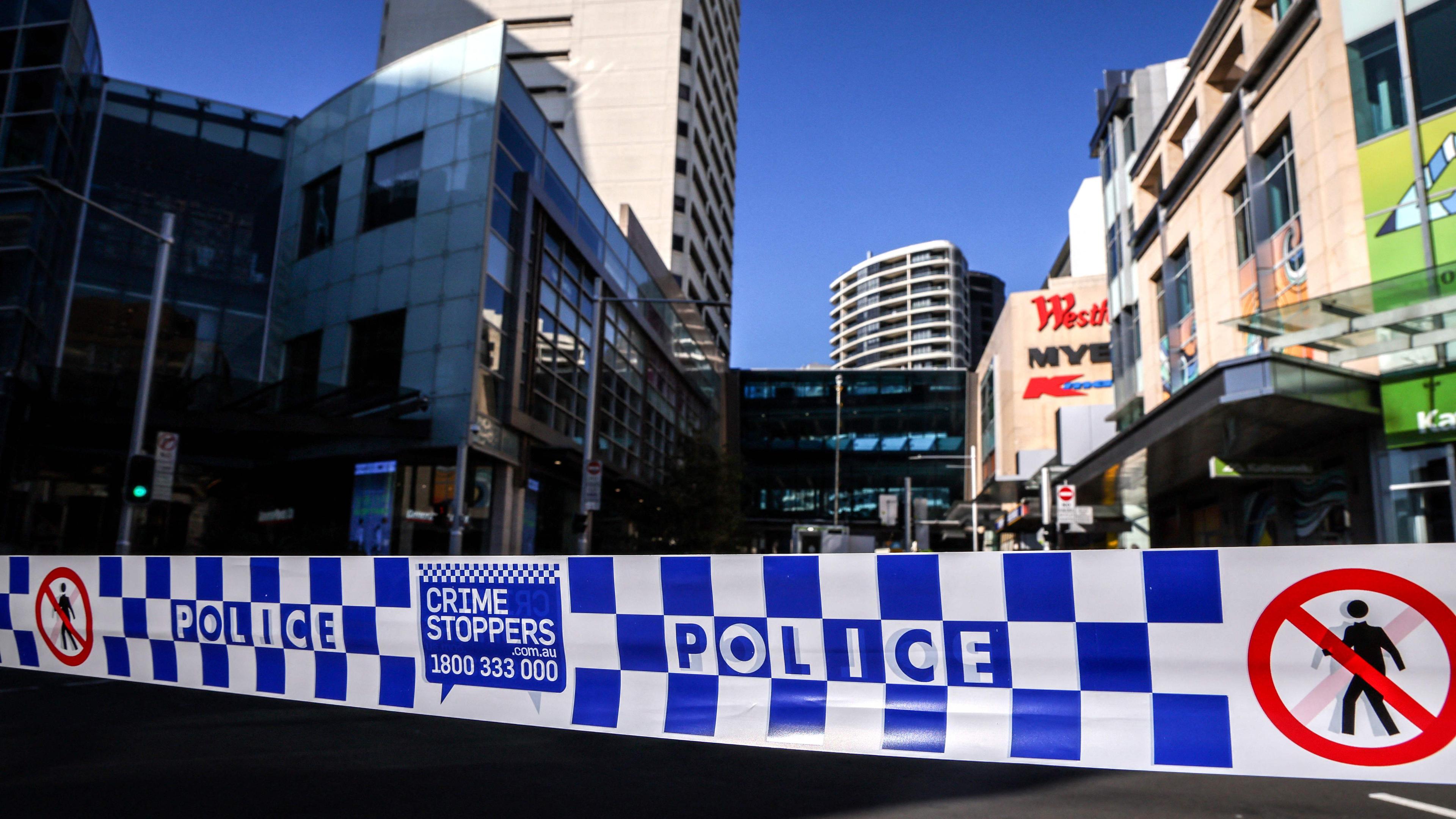 Police tape can be seen in front of a roadblock outside the Westfield Bondi Junction shopping mall in Sydney on April 14, 2024, the day after a 40-year-old knifeman with mental illness roamed the packed shopping centre killing six people and seriously wounding a dozen others. (Photo by DAVID GRAY / AFP)