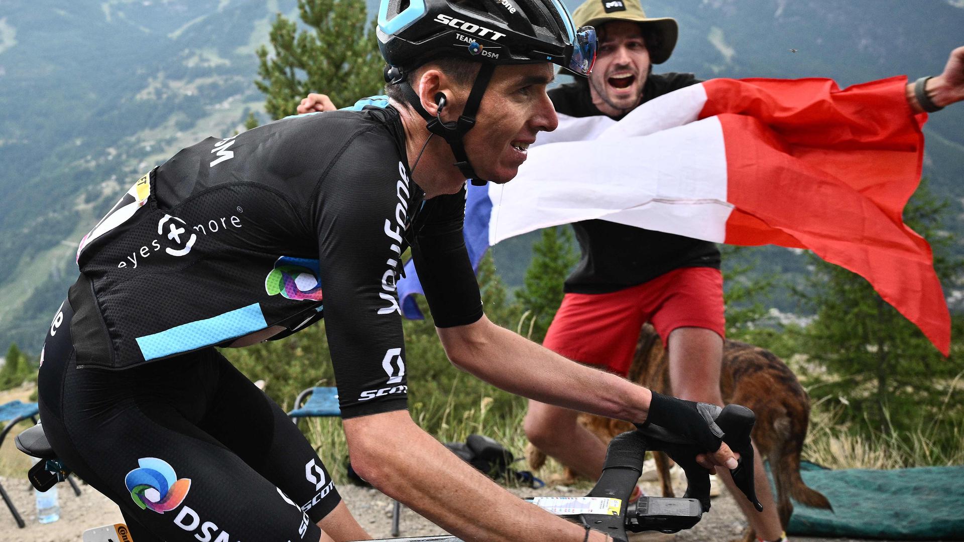A spectator reacts with a French flag as Team DSM team's French rider Romain Bardet (L) cycles during the 11th stage of the 109th edition of the Tour de France cycling race, 151,7 km between Albertville and Col du Granon Serre Chevalier, in the French Alps, on July 13, 2022. (Photo by Marco BERTORELLO / AFP)