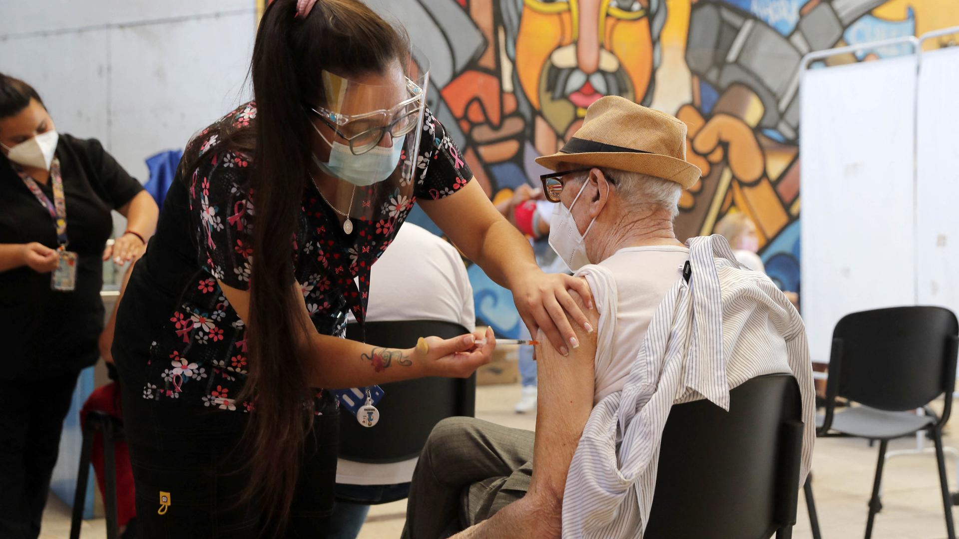 An elderly man receives a BioNtech Pfizer Covid-19 jab as a booster, in Santiago, on February 7, 2022. - Chile began vaccination on Monday with the fourth dose against covid-19, for  people over 55 years of age, in the midst of a wave of infections. (Photo by JAVIER TORRES / AFP)