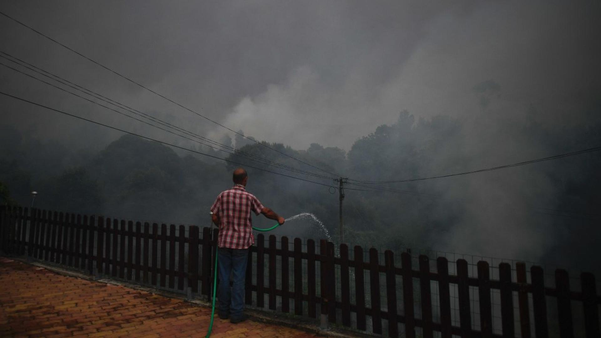 Un habitant du village de Trespostos essaie d'éteindre le feu qui encercle des maisons à Figueiro dos Vinhos, à l'aide d'un tuyau.