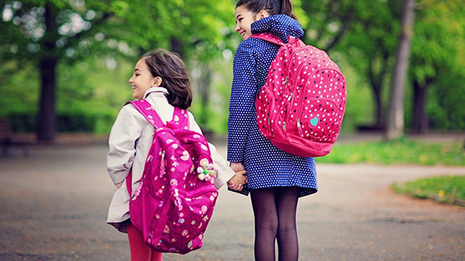 Two sisters are going to the school pass throught the local park.